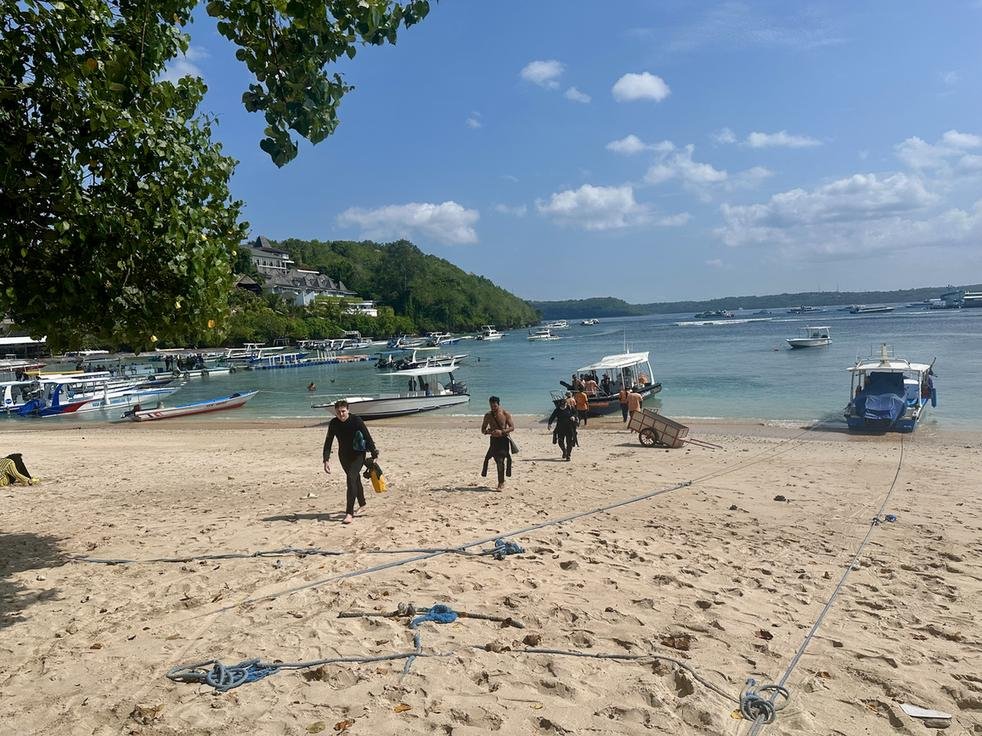 Scuba divers disembarking from a dive boat onto the beach at Toyapakeh, Nusa Penida