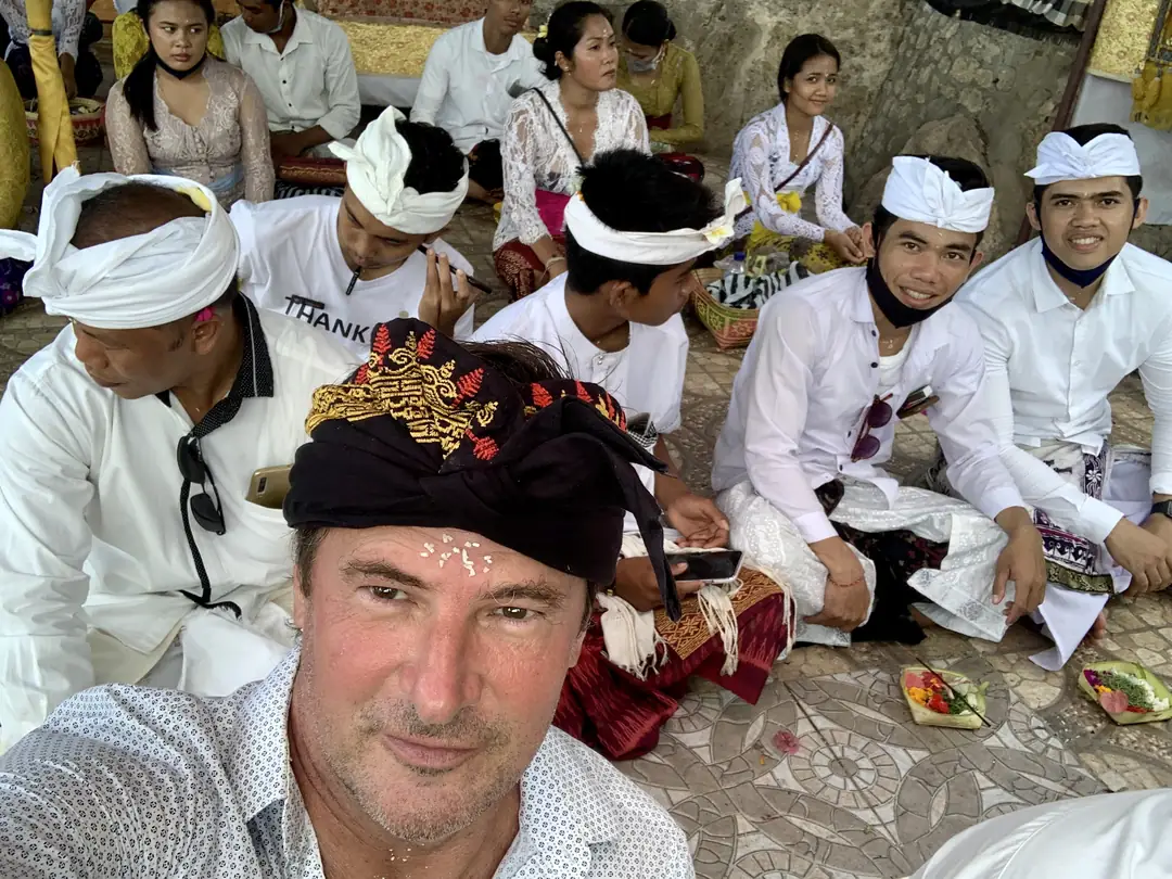 Blaise Jaeger sitzt zwischen balinesischen Gläubigen in weißer Kleidung, mit geweihten Reiskörnern auf der Stirn, während einer Zeremonie in Goa Giri Putri, Nusa Penida
