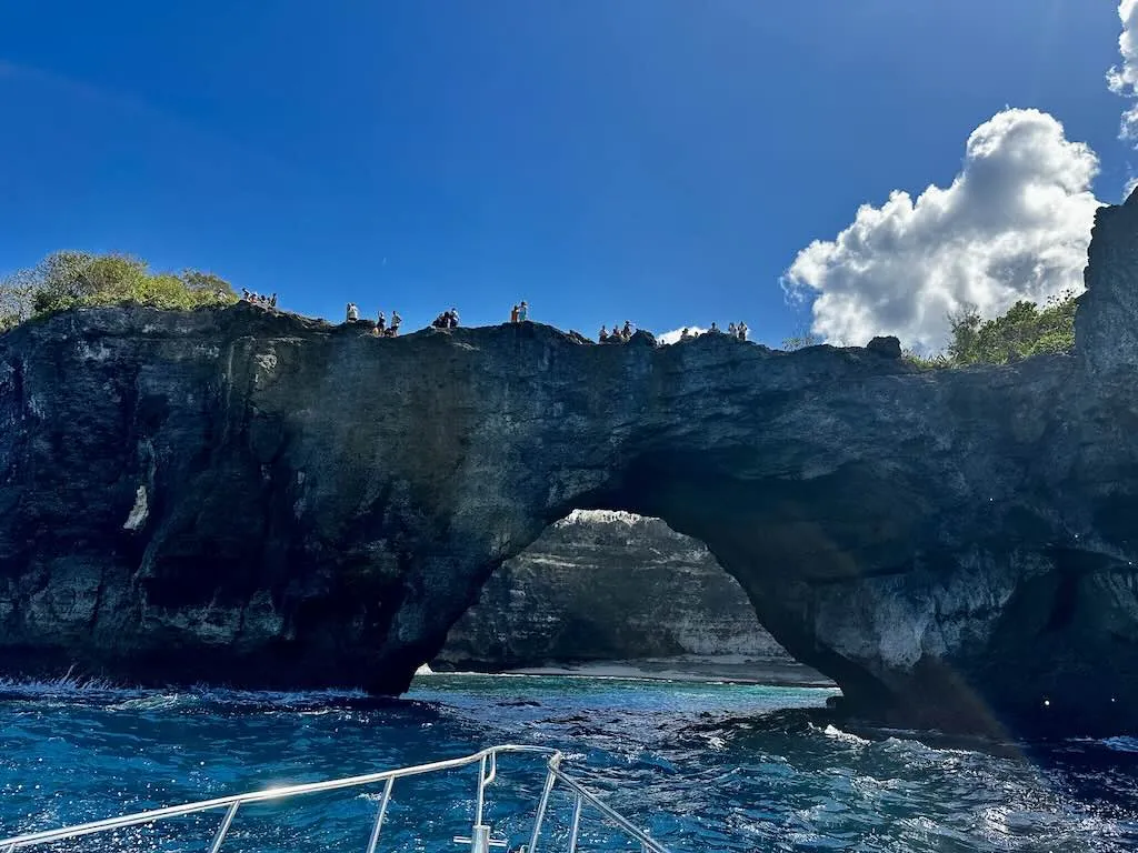 Lengkungan Broken Beach dilihat dari perahu selam dengan wisatawan di puncak tebing, Nusa Penida