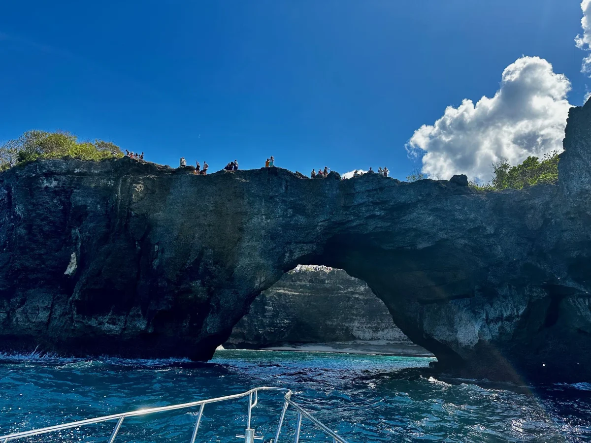 The Broken Beach arch from a dive boat with a crowd of visitors on the clifftop above, Nusa Penida