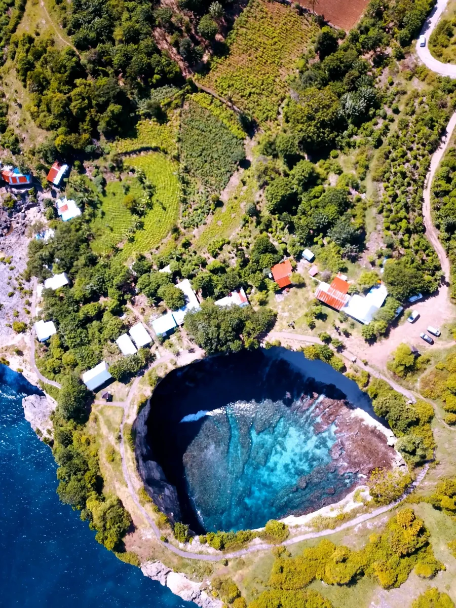 Aerial view of the circular bay of Broken Beach surrounded by warungs, tracks and farmed plots, Nusa Penida
