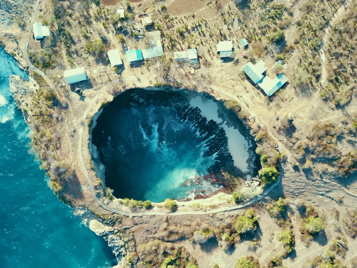 Aerial view straight down onto the circular bay of Broken Beach, Nusa Penida, with swell surging through the tunnel