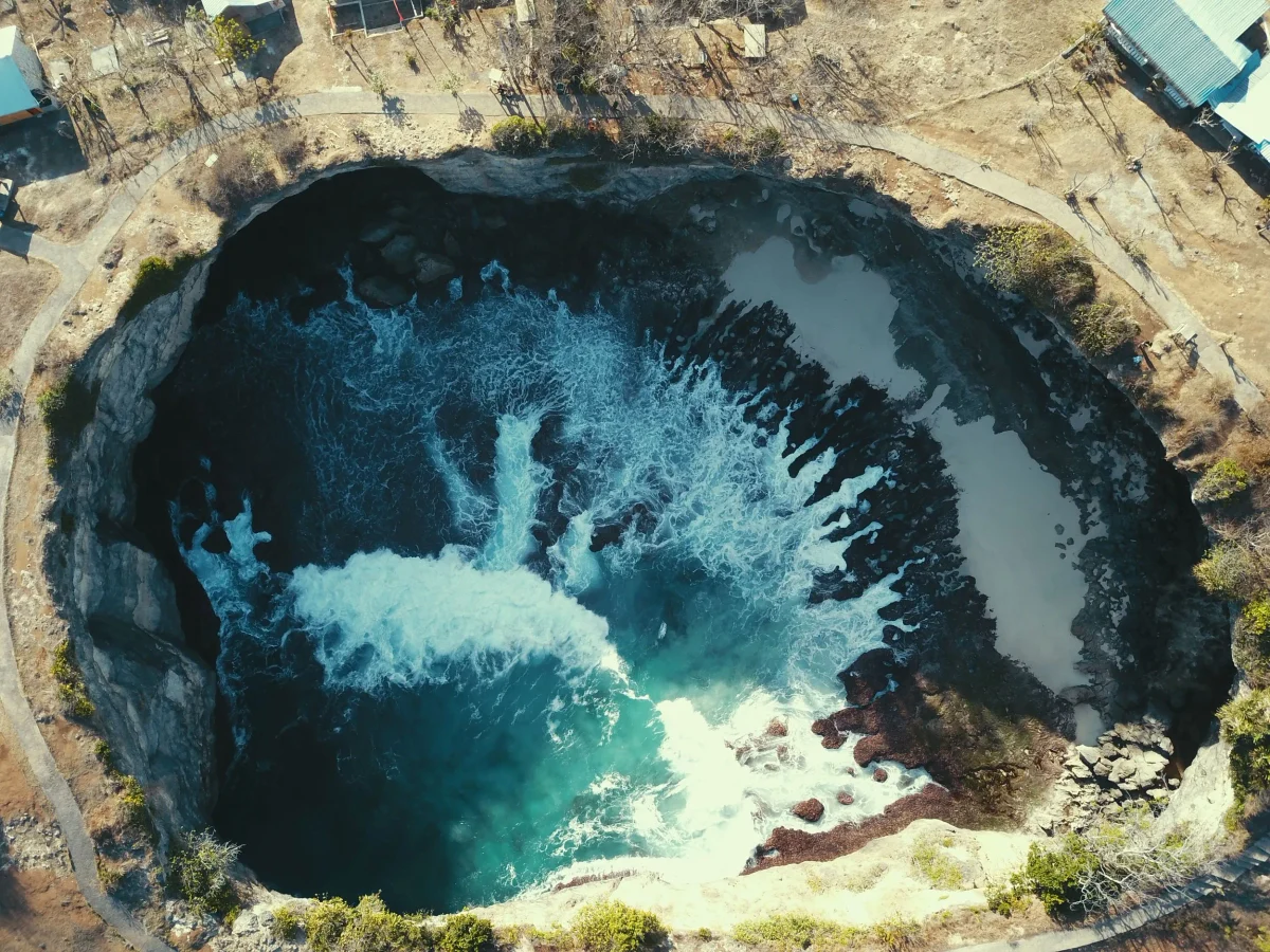 Swell breaking through the rock tunnel into the circular bay at Broken Beach, seen from a drone, Nusa Penida