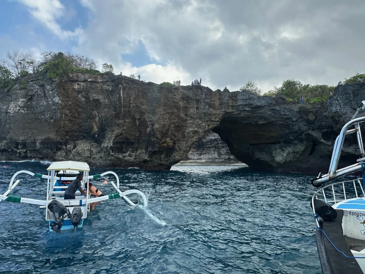 Traditional Balinese jukung outrigger holding position at Manta Bay with snorkelers in the water, below the Broken Beach cliffs, Nusa Penida