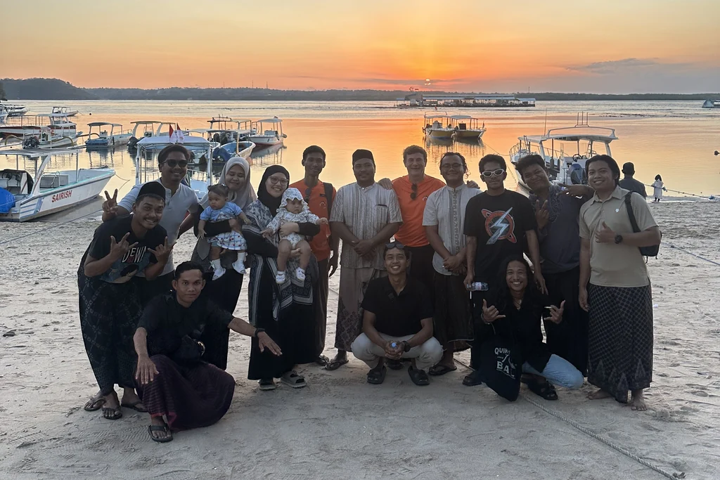 El equipo de buceo de Dune Penida y sus familias compartiendo una comida en la playa de Toyapakeh al atardecer, Nusa Penida