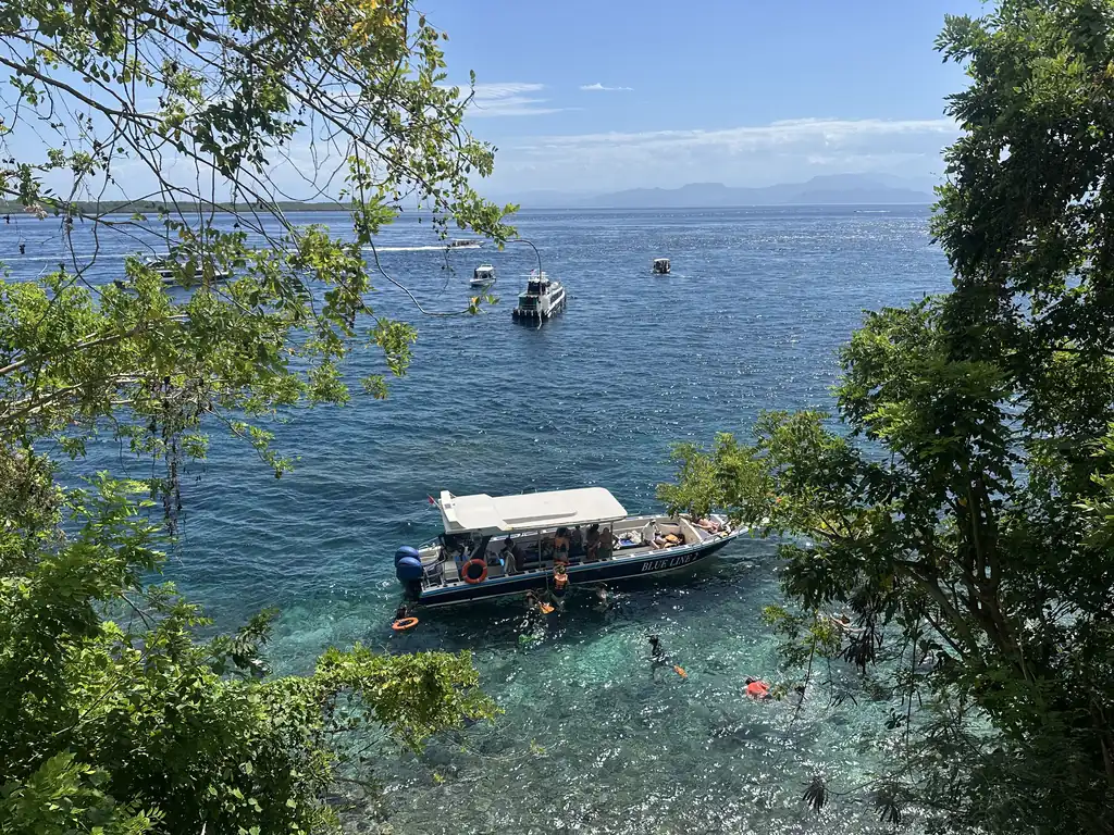 Personas haciendo snorkel sobre la pared de coral bajo Adiwana Warnakali, vigiladas desde su barco, Toyapakeh, Nusa Penida