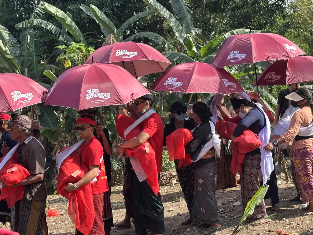 Family members carrying wrapped remains beneath a ceremonial parasol during Ngaben