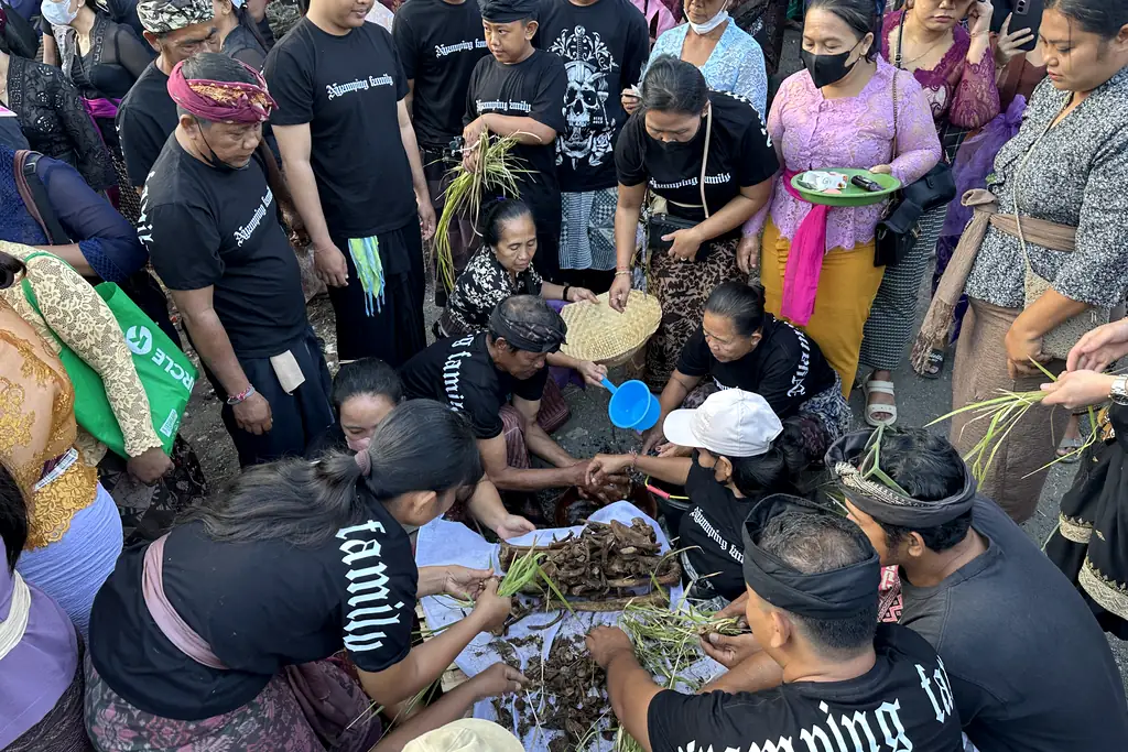 Family members cleaning bones with water and alang-alang grass during Ngaben in Sebunibus