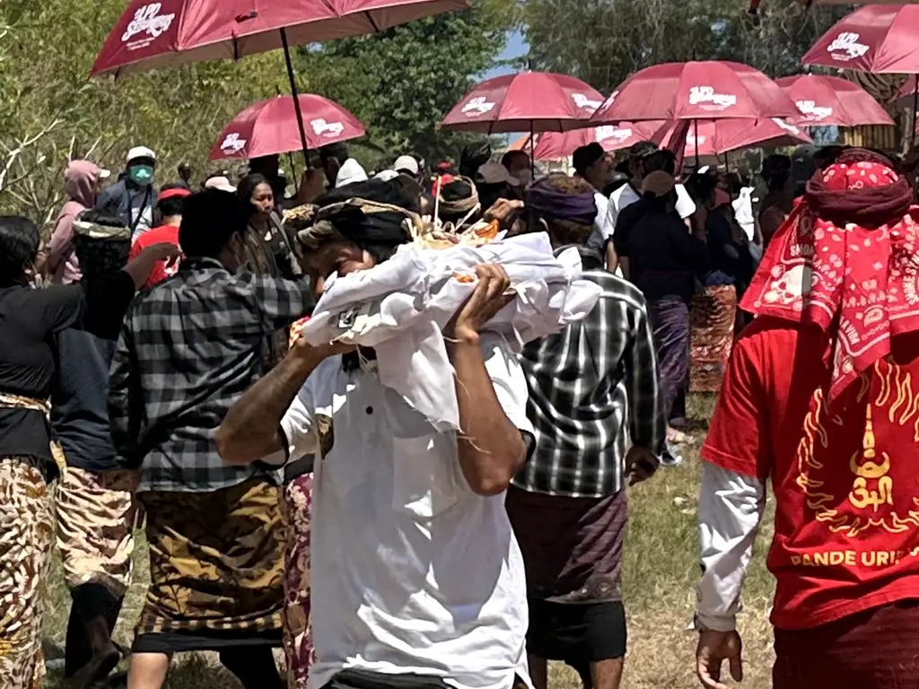 Family member carrying wrapped remains after they are lowered from the ceremonial tower during the Sebunibus Ngaben